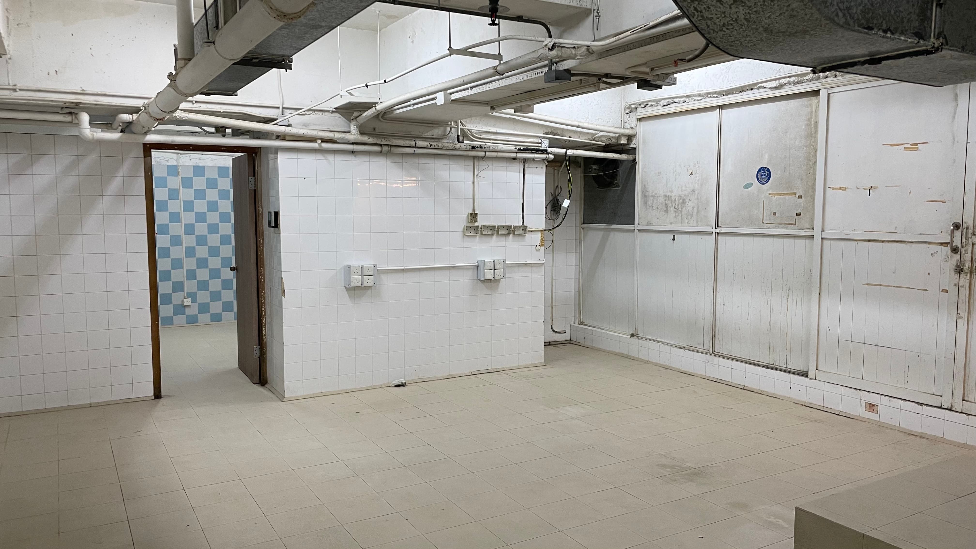 Ref#3494: Spacious bare room with white tiled walls, beige floor, and exposed ceiling pipes
d�ideal for shop or restaurant rental. Features doorway to blue and white checkered room; walls and fixtures show signs of wear.