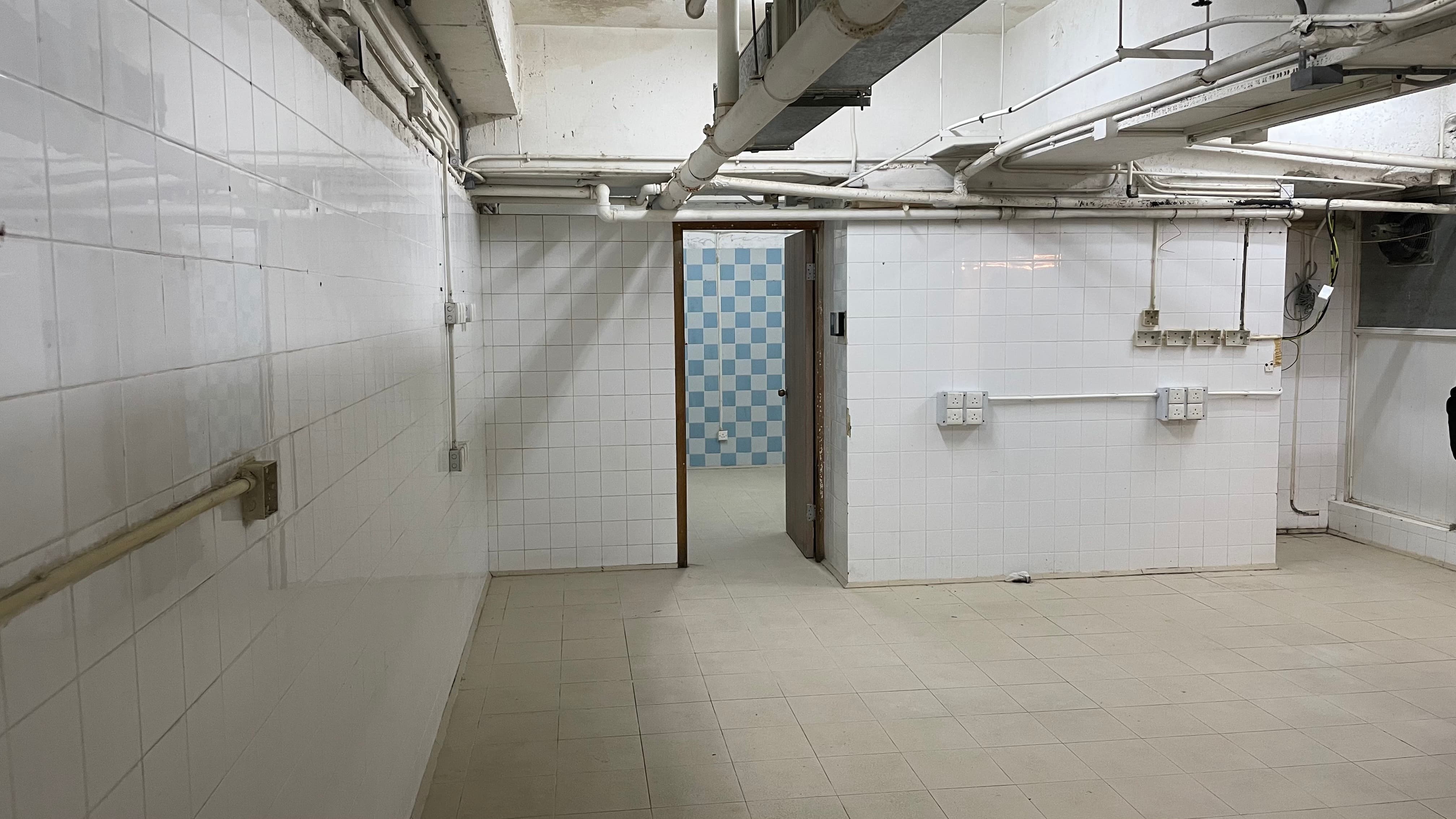 Ref#3494: Brightly lit, tiled basement room with exposed ceiling pipes. Features a back doorway to a blue and white checkered area. Ideal for shop or office rental.