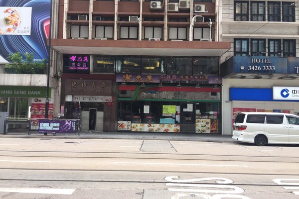 Street view featuring Ref#3177: shop rentals, restaurants with colorful Chinese and English signs, hotel entrance, a white van, and a bank along a city sidewalk with tram lines in the foreground.