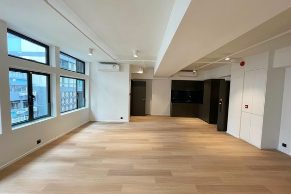 Ref#3530 offers a spacious, modern unfurnished room ideal for an office, featuring light wooden floors, large left-side windows for natural light, white walls, and a built-in black entertainment unit on the far wall.