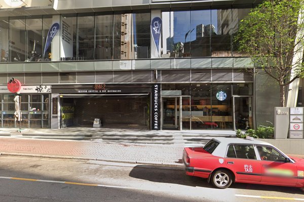 A red taxi is parked on the street outside a modern building with glass windows, home to Starbucks and another restaurant with a shutterideal for renting shop or restaurant space like Ref#3451.