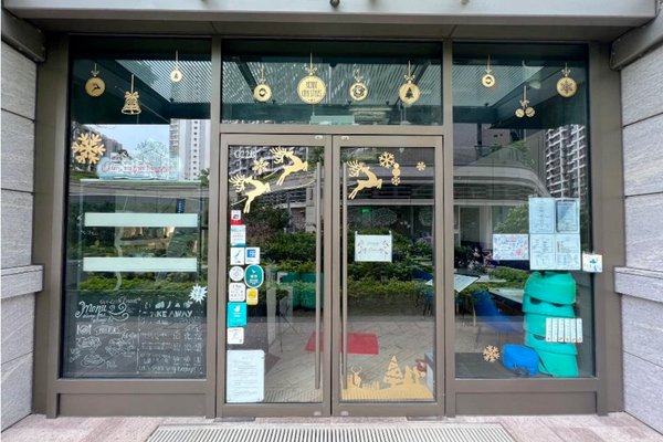 Ref#3428: Storefront for rent with glass doors decorated with gold holiday ornaments, reindeer, and snowflakes. Doors display signs, menus, and stickers. Green plants and buildings are visible outside.