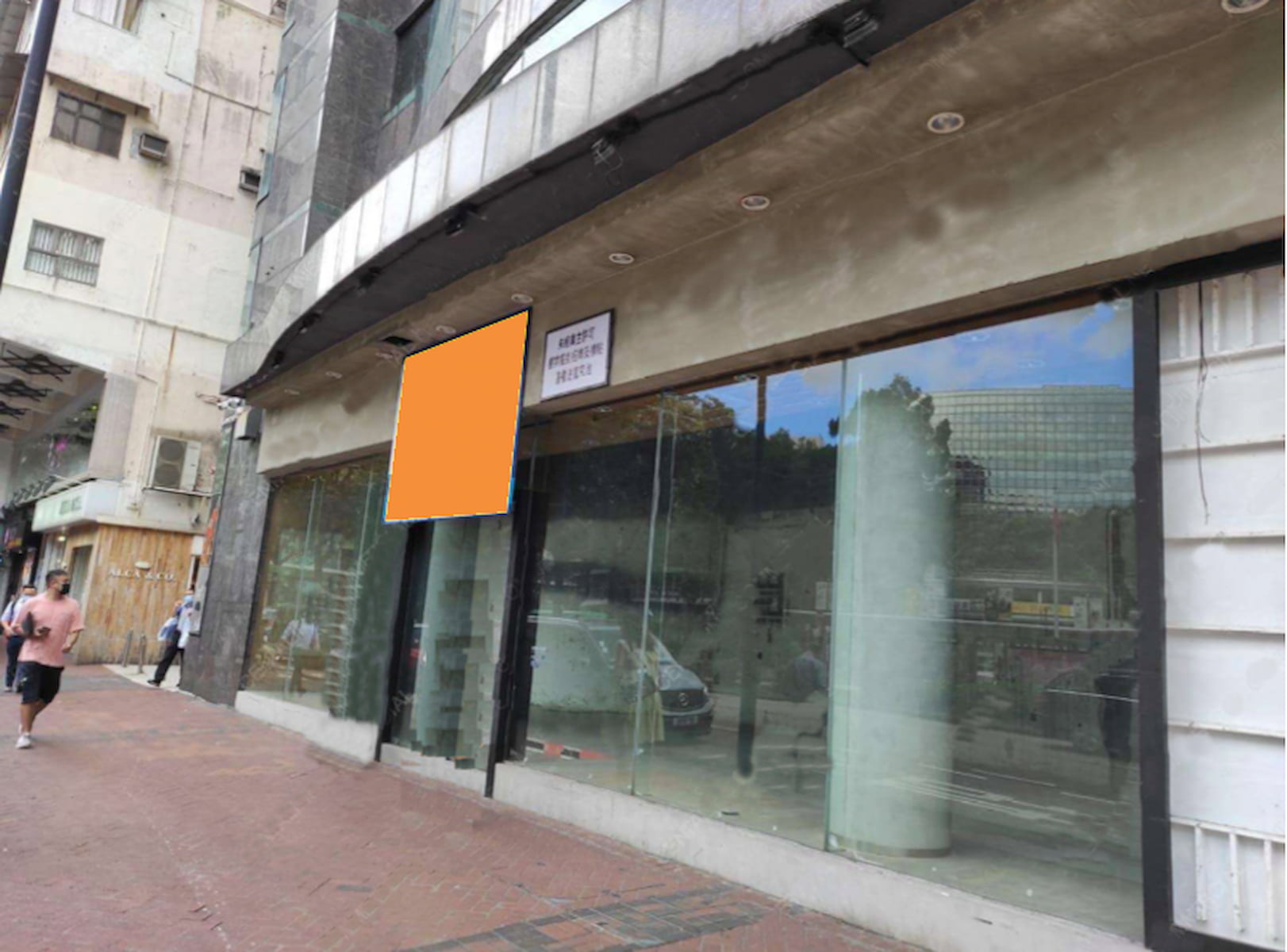 Ref#3228 is a vacant city storefront with large glass windows and blank signage, ideal for shop rental. Pedestrians walk past its worn exterior, which reflects nearby buildings in the glass.