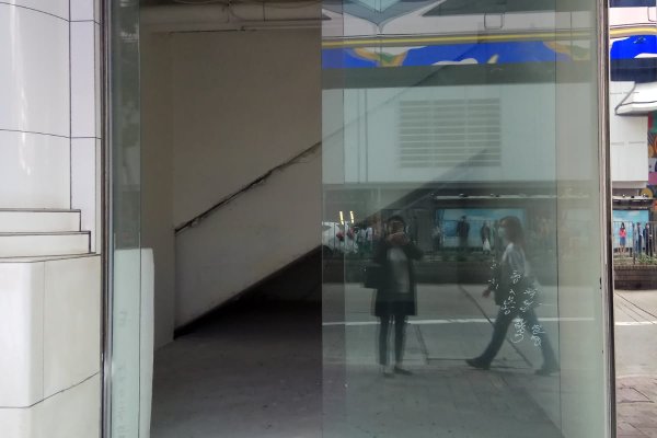 Ref#3426 features a glass window reflecting two people on the sidewalk. Inside, an empty room with a slanted staircase suggests rental potential, while outside, urban street elements and buildings are visible.