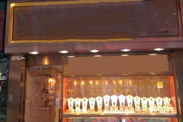Ref#3576: A jewelry store with a gold-toned exterior and a bright display window features elegant necklaces and jewelry on stands—an ideal shop rental. The store’s name and signage are intentionally blurred and unreadable.
