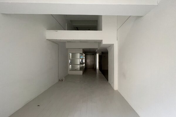 Ref#3514 is a narrow, white-walled room with exposed beams and a white wooden floorideal to rent for office or shop use. Features include a small bucket on the left and a glass surface mounted on the rear left wall.