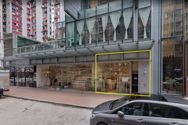 Street view of Ref#3385, a modern glass-fronted shop rental with large windows. Part of the storefront is outlined in yellow, with a parked car and moving truck in front and tall buildings in the background.