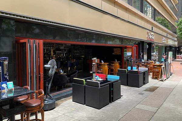 Ref#3319 features a modern bar or café with an outdoor seating area, tables, chairs, and a partially open wall to the indoor bar—perfect for restaurant rental—located on a lively city street sidewalk.