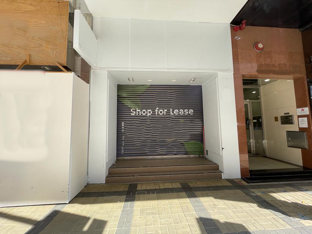 Ref#3331: Closed storefront with a metal shutter displaying Shop for Lease—ideal for renting shop or office space. Surrounded by white walls and tiled sidewalk.
