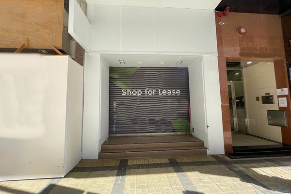 Ref#3331: Closed storefront with metal shutter marked "Shop for Lease"—perfect to rent as shop or office space. Features steps at entrance, located between two buildings with tiled sidewalk in front.