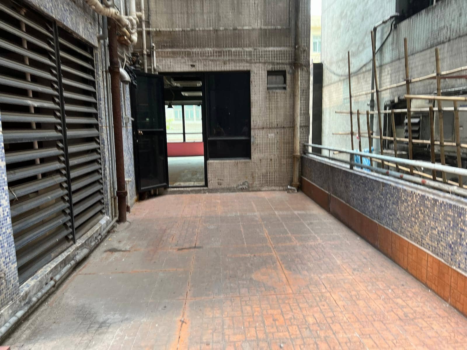 銅鑼灣渣甸街兩座建築物之間的鋪瓷磚戶外行人道,一道黑色門微開,右側可見棚架。
