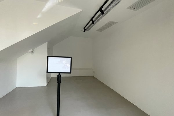 Ref#3314 is a small, empty white room with a sloped ceiling, grey floor, and mounted surveillance cameraideal to rent as an office or shop. A black stand with a monitor in the center adds a modern touch.