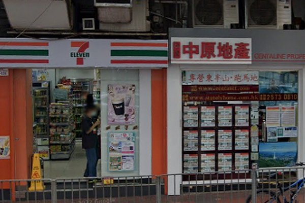 A person stands at the entrance of a 7-Eleven beside a real estate agency with Chinese signage, where Ref#3585 and other property listings for office or shop rentals are displayed in the window.