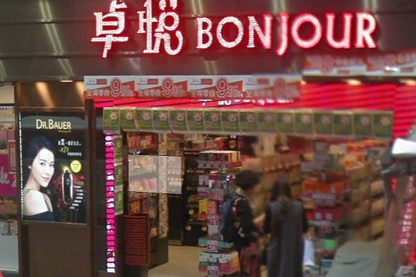 Ref#3230: Bonjour shop storefront with bright red signage and Chinese characters above the entrance. Posters, products, and a Dr.Bauer ad are visible; two people browse—perfect for renting shop or office premises nearby.