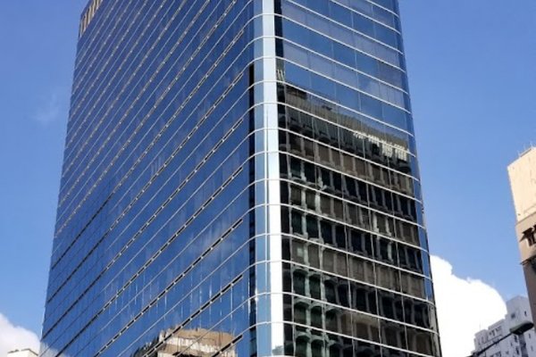 Ref#3150 is a tall, modern glass office building with reflective windows, offering rental office space and beautiful views of neighboring structures and clouds against a blue sky.
