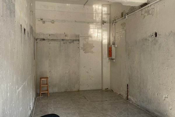Ref#3443: Spacious room with tiled floor, exposed pipes, and a wooden stool2perfect for office or shop rental. Sunlight brightens the space through a window, enhancing its potential.