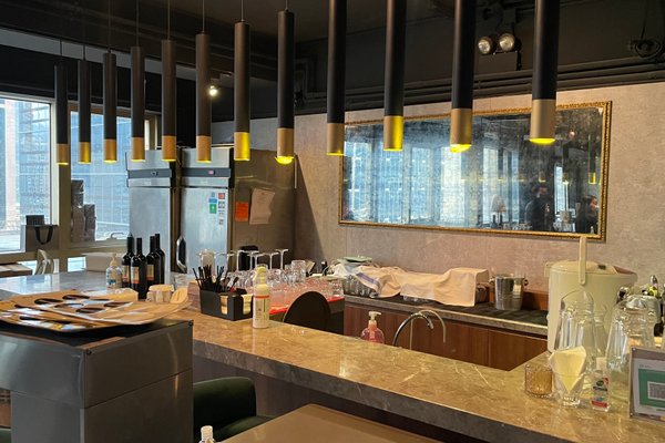 Ref#3195: A modern bar with a marble counter, hanging black and gold pendant lights, wine bottles, glassware, refrigerators in the background, and a large mirror above the counter

ideal for restaurant rental.