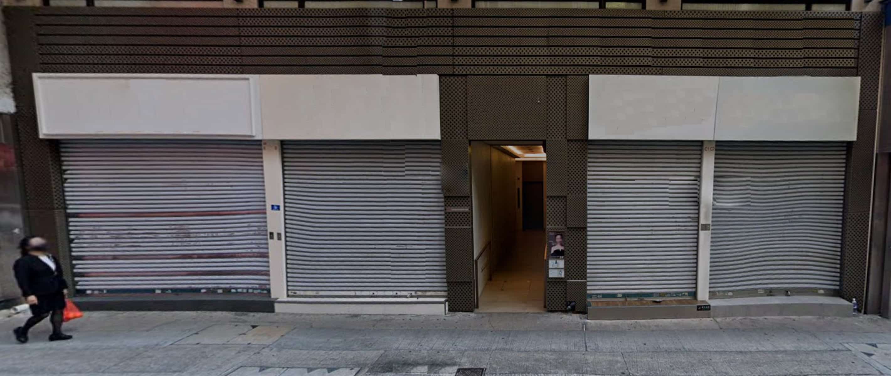 A person in a mask walks by Ref#3247—a closed storefront with metal shutters and a central, narrow entrance—an ideal city location to rent shop or lease restaurant space.