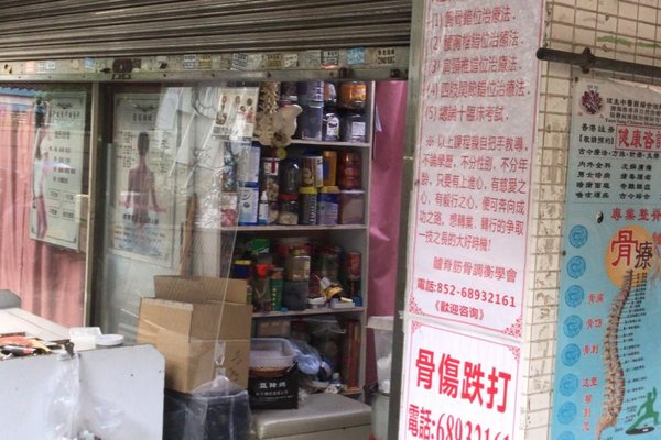 Ref#3512: A shop entrance filled with jars, boxes, and items; Chinese signs and posters by the door. Ideal for those seeking rental space. Metal shutter is partially down.