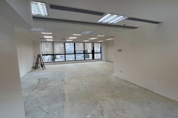 Ref#3405: Bright empty office space with white walls, large windows, and concrete floorsideal for office or shop rental. Ceiling lights are on, with folded chairs and a ladder near the windows.