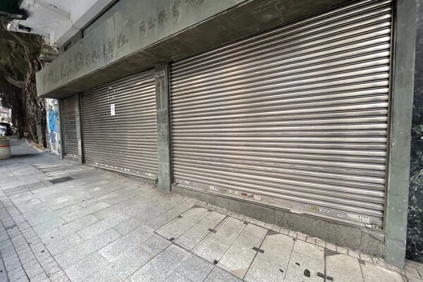Ref#3172: A sidewalk in front of a closed storefront with three large metal shutters down. This quiet, empty urban space is ideal for anyone looking to rent a shop or restaurant in the city.