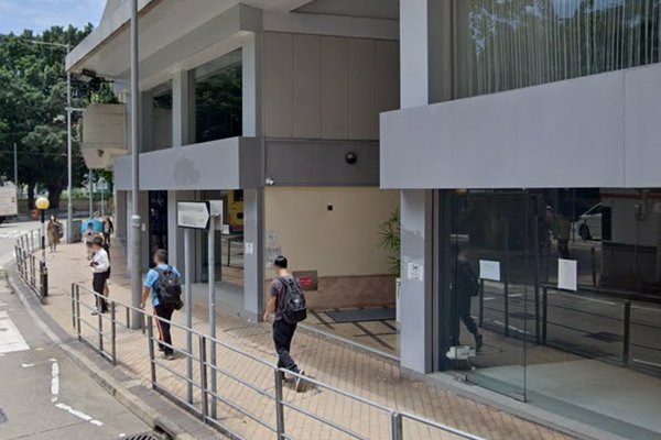 Three people walk past Ref#3471, a modern glass-fronted building with railingsideal for those seeking shop or office space. Trees and street signs can be seen in the background.