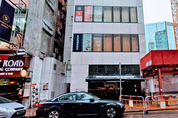 A black car is parked on a city street in front of a modern white building with signs like BN, SUSHISHU, and a menu. Ref#3433 is ideal for those seeking to rent restaurant or shop spaces. Surrounding buildings and a crane are visible.