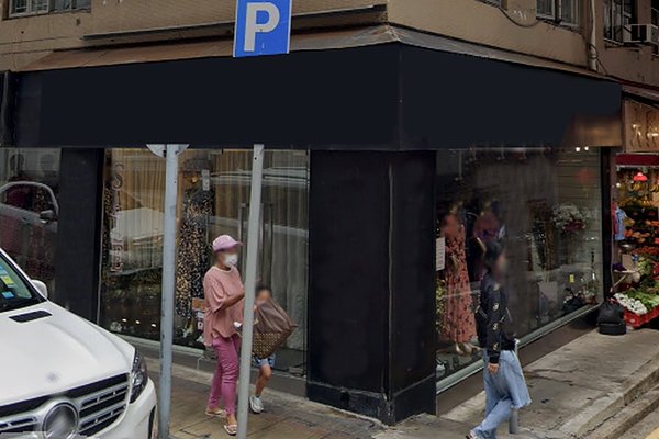 A woman in pink and a child walk past Ref#3468, a corner clothing store with black signage and large windows for rent; a white car is parked nearby, and a blue parking sign is visible.