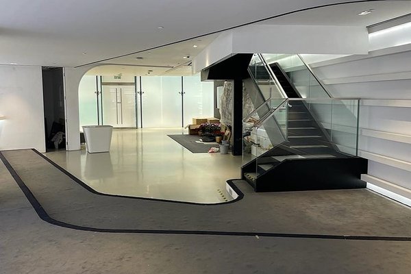 Ref#3203 offers a modern, minimalistic lobby for office or shop rentals, featuring a glass-walled staircase, white walls, sleek floors, scattered plants, and abundant natural light streaming through frosted glass doors.