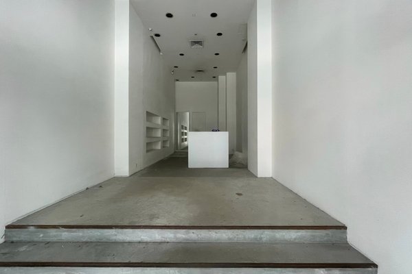 Ref#3475: Minimalist white room with concrete floor, short stairs, recessed ceiling lights, left wall shelves, and a white counter before a mirrorperfect for rent as an office or shop.