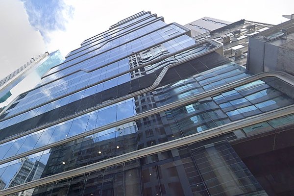 Ref#3594: A modern glass skyscraper with angular lines and many windows, reflecting nearby buildings and sky10ideal spaces for office, shop, or restaurant rental beneath a partly cloudy sky.