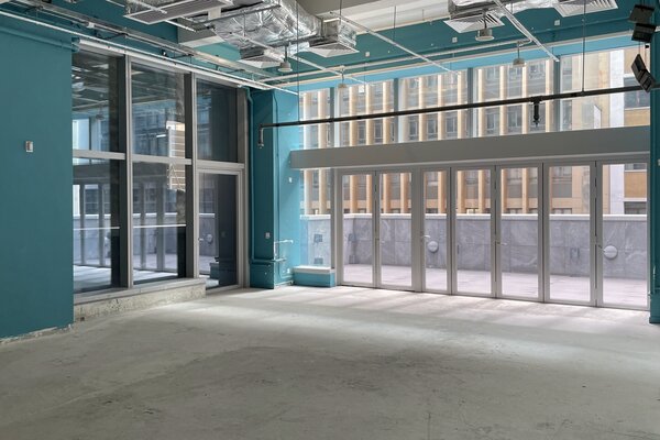 Ref#3563: Spacious, modern room with teal walls and large windows perfect for office rental. Features glass doors to a balcony with city views and exposed ducts for an industrial urban vibe.