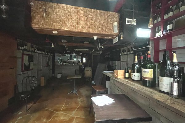 Ref#3567: A dimly lit, rustic bar with vintage charm wooden counter, shelves lined with bottles, and empty tables ideal to rent as a unique restaurant or trendy shop.