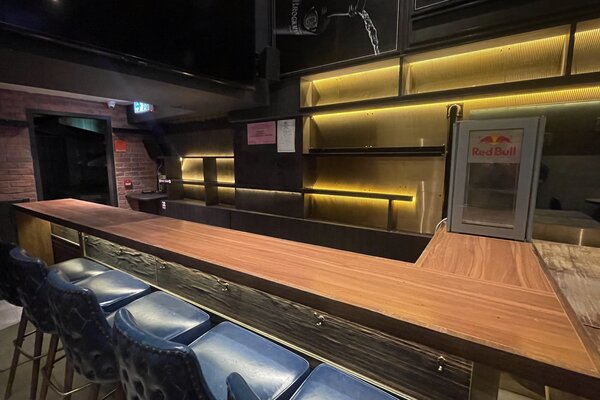 Ref#3538: A clean, stylish modern bar for rent as a shop or restaurant, featuring a wooden countertop, dark blue barstools, empty shelves with warm lighting, and a Red Bull fridge—ready for your business vision.