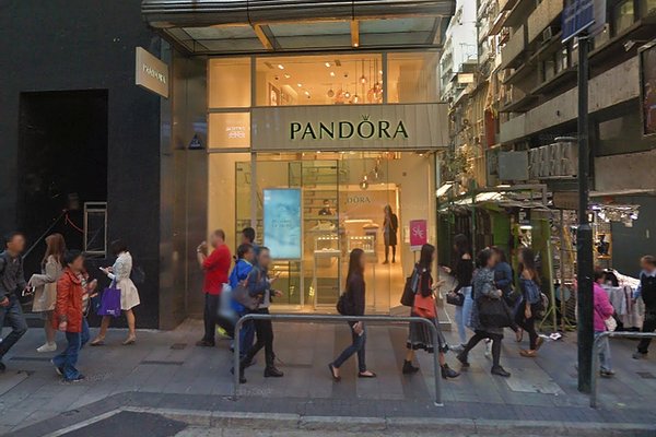 People walk past the brightly lit Ref#3168 jewelry store on a bustling city street lined with modern shops and glass windows, near office and shop rental spaces, making the area vibrant with activity around the clock.