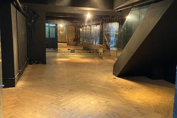 Ref#3220: An empty room with wooden herringbone floors, black walls, glass panels, and exposed brick

ideal to rent as a restaurant or shop. Overhead lights reflect beautifully off the shiny surfaces.