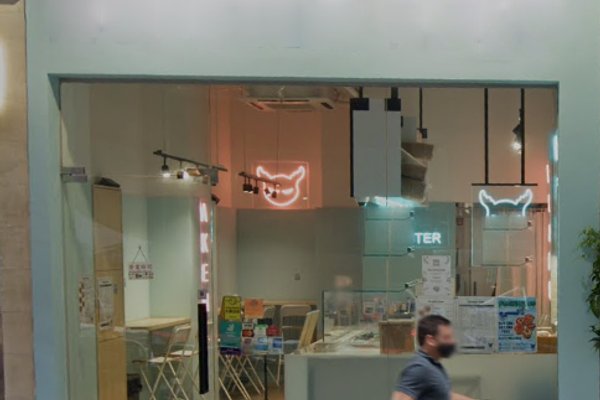 Storefront Ref#3363 features large glass windows and a modern, minimalistic interior2�1deal for shop or restaurant rental. A cat face-shaped neon sign glows inside as a person passes the entrance outside.