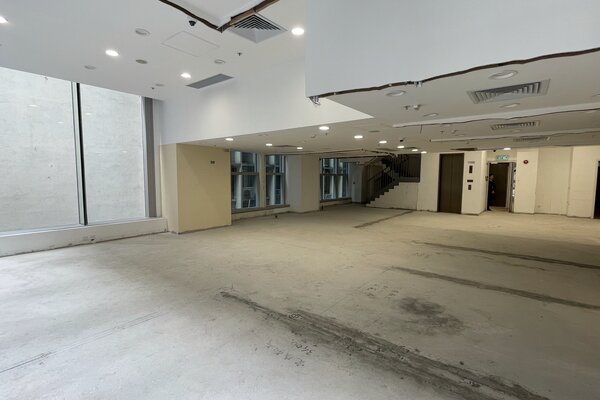 Ref#3532: Spacious indoor area with bare floors, white walls, ceiling lights, exposed vents, a staircase, and large windows for natural light—perfect to rent as a shop or office.
