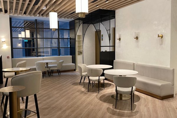 Ref#3588: A modern, minimalist cafe interior for restaurant rental with light wood floors, white cushioned seating, round tables, and pendant lights. Large windows and a mirror enhance the open, airy feel.