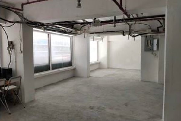 Ref#3367: An unfinished room with white walls, exposed ceiling pipes, and large windows for natural lightideal for office rentalfeatures a small desk, chair, and computer in one corner.
