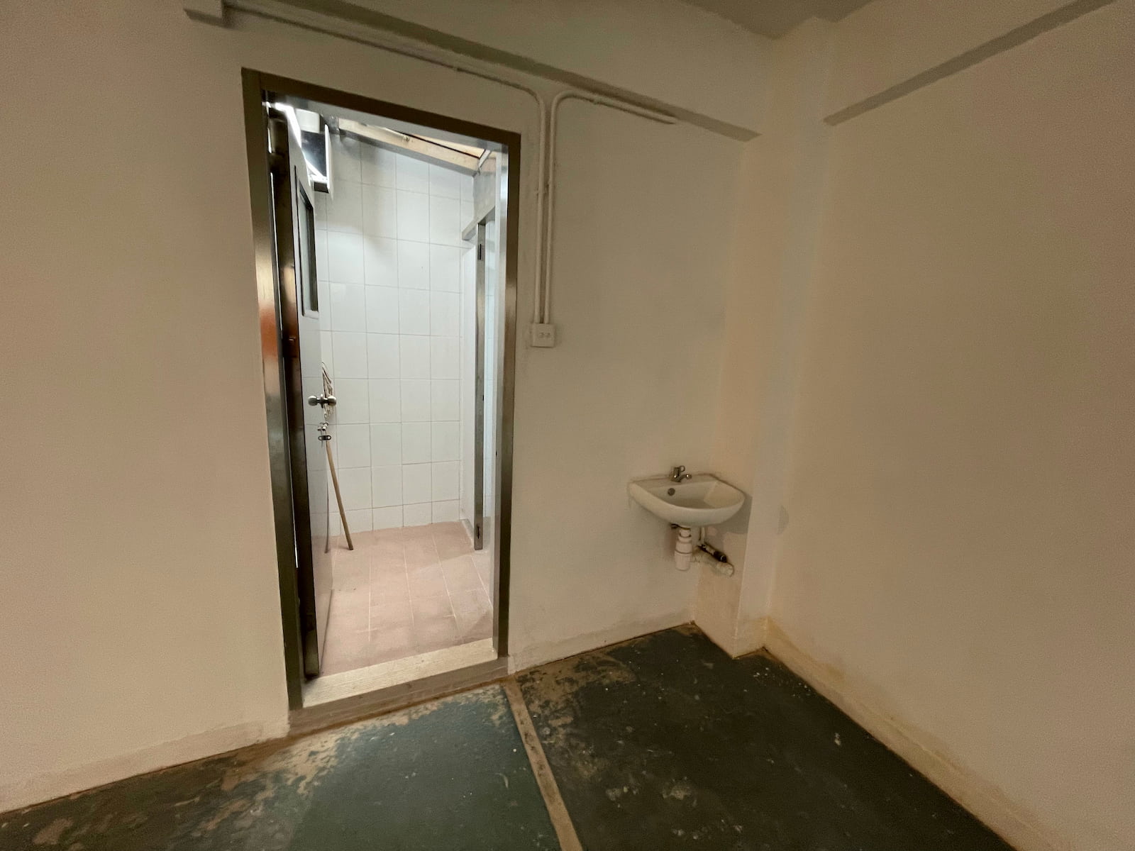 Ref#3587: Small empty room ideal for a shop or office, with a sink on the right wall, a door to a tiled shower area, unfinished flooring, and plain walls.