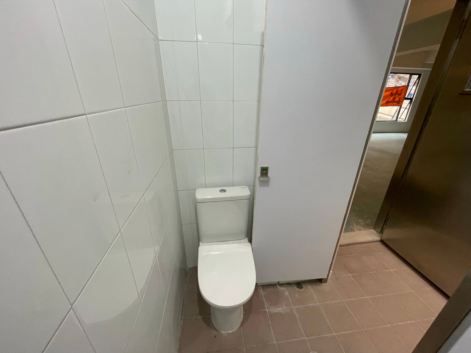 Ref#3587: Small bathroom with white tiled walls and a white toilet near the door, which opens to a larger unfinished room1perfect for renting as office or shop space.