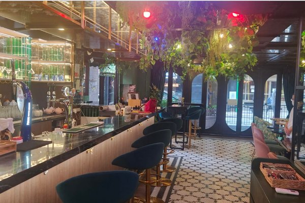 Ref#3305: A stylish bar with green velvet chairs, black marble counter, hanging plants, and geometric floor tiles

ideal for shop or restaurant rental. Warm lighting highlights shelves of bottles behind the bar and large windows greet guests.