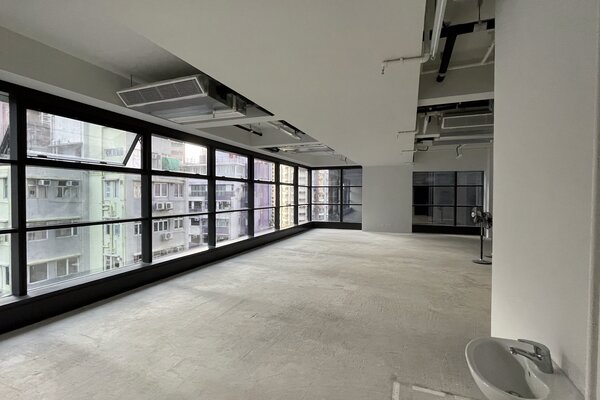 Ref#3266 is a spacious, empty room with floor-to-ceiling windows on two sidesideal for an office or shop. It offers abundant natural light, a concrete floor, exposed ceiling pipes, and a small white sink in the corner.