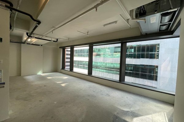 Ref#3410 is an empty office space ideal for rent, featuring large floor-to-ceiling windows, concrete floors, and exposed ceiling pipes. The room overlooks modern office buildings and is filled with natural light.
