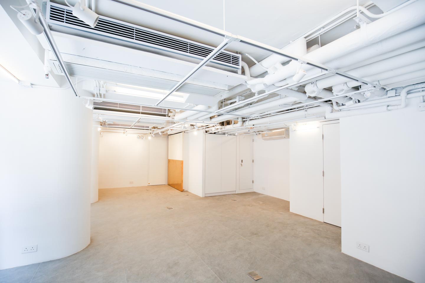 Ref#3489 features a spacious, empty room with white walls, exposed ceiling pipes, gray tiled floors, large pillars, and multiple doors—perfect for an office or shop rental. Modern industrial style with bright lighting throughout.