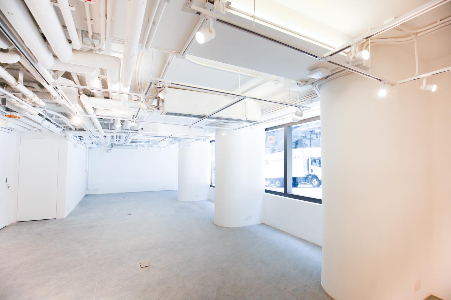 Ref#3489 is a bright, empty room with large windows, white walls, and exposed ceiling pipes. Natural light enhances its modern industrial style—perfect to rent as a shop or office.
