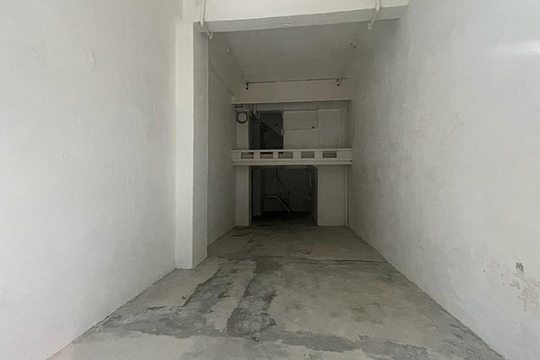 Ref#3456: An empty, narrow room with bare concrete floors, white walls, and a small rear mezzanine. Overhead pipes and exposed wiring create an industrial vibe
perfect to rent as a shop or office. Dimly lit for a unique atmosphere.
