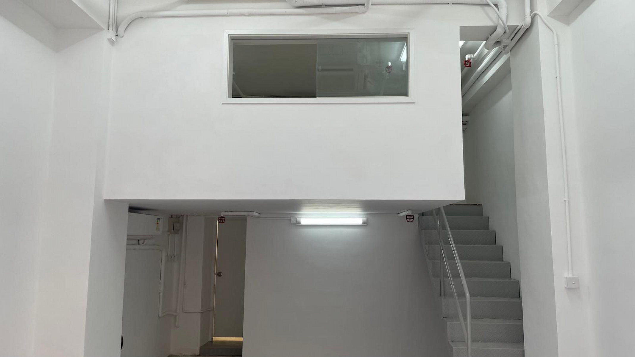 Ref#3038 features a white, minimalist interior with a small staircase to a loft with a window1 perfect for renting as an office or shop in a clean, brightly lit space enhanced by fluorescent lighting.