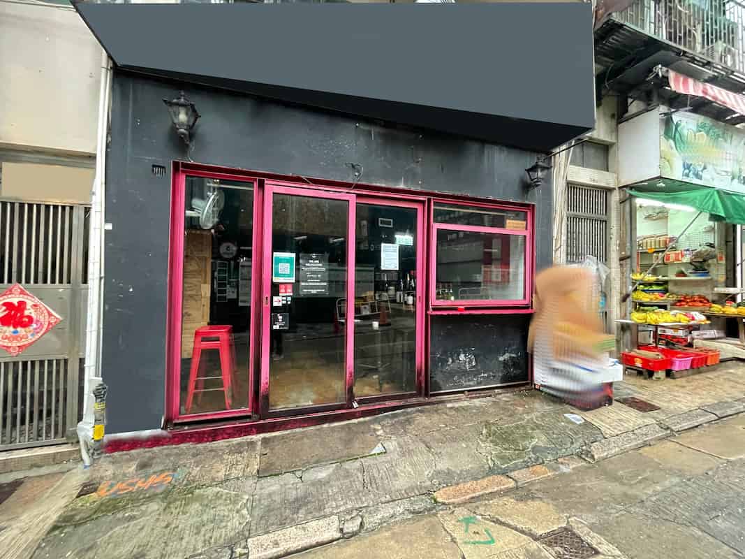 Ref#3036: Storefront with large glass windows, black facade outlined in redideal for shop rental. Features two lantern lights above and fresh produce displayed on the right. Wet sidewalk, passerby included.